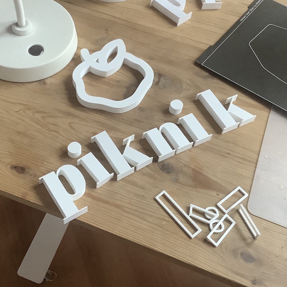 Druk 3D - białe litery i logo Studia Piknik na drewnianym blacie